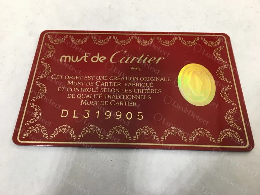 A genuine red Must de Cartier card with a gold seal and a card number of two letters followed by six digits
