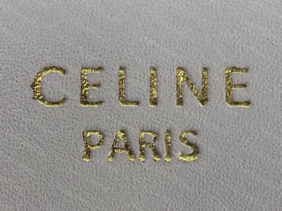 Counterfeit heat stamp on a white Classique Triomphe: grainy, patchy foil with ragged edges and letters spread too wide.