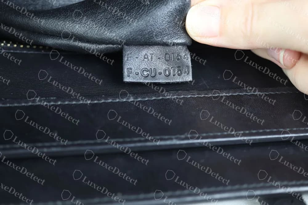 Una linguetta originale di una Celine Mini Luggage con un codice su due righe stampigliato su una piccola pelle nera: F-AI-0154 sopra F-CU-0154