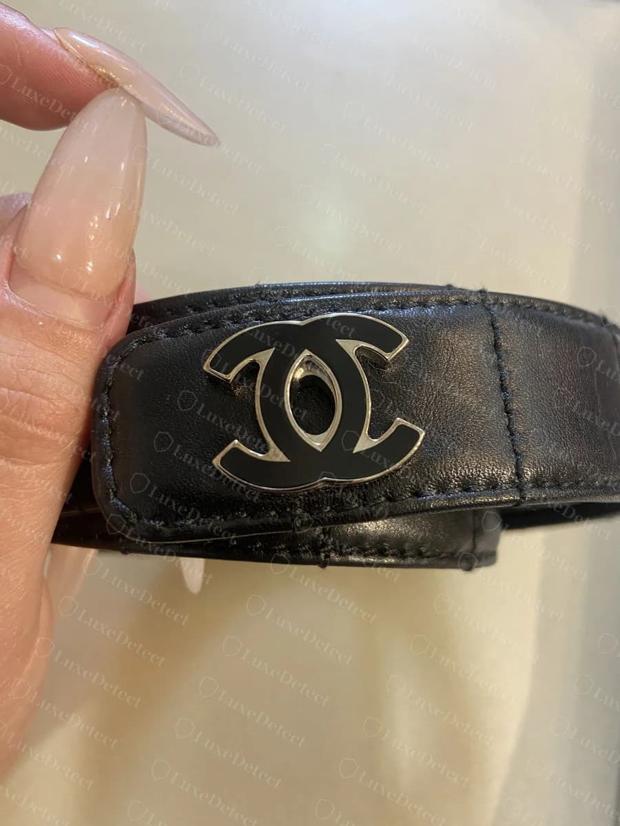 Genuine Chanel enamel CC logo plaque stitched onto a leather tab on a black belt, showing the clean enamel fill and consistent stitching around the tab