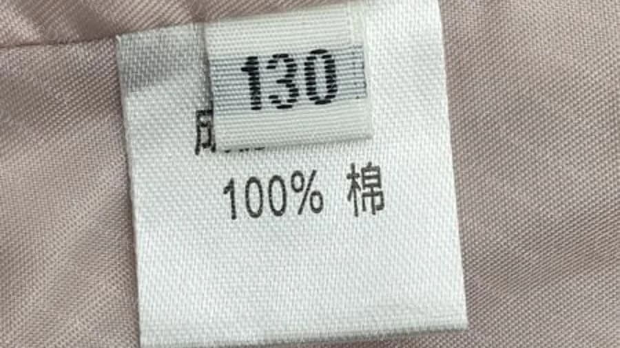 Fausse étiquette avec une étiquette de taille numérique tissée 130 au-dessus d’une ligne de composition uniquement en chinois indiquant 100 pour cent coton