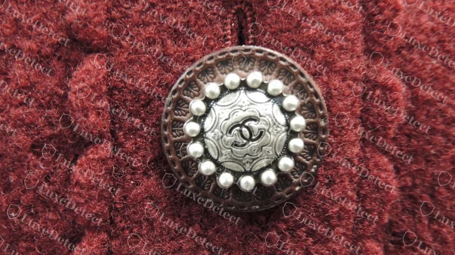 Bouton Chanel authentique avec un médaillon double C couleur étain cerclé de perles, sur une veste en laine rouge
