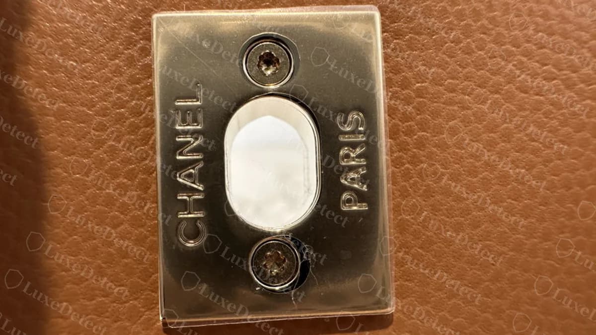 Placa trasera del cierre giratorio de un Coco Handle original: una placa rectangular de metal con CHANEL y PARIS grabados a cada lado de una abertura ovalada, con dos tornillos