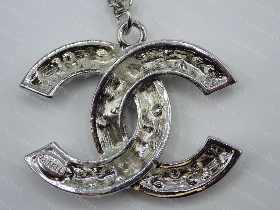 Counterfeit Chanel pearl CC pendant from the back, a hollow recessed channel with every stone seat showing through as a cast bump, and a small cartouche reading only "CHANEL" in one corner