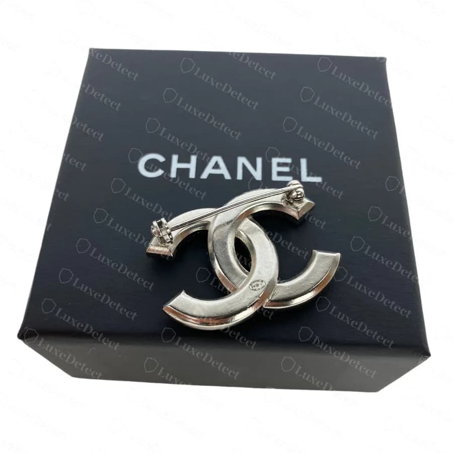 Genuine Chanel crystal CC brooch seen from the back, a closed, smooth metal surface with the small plaque set in and the pin and safety catch across the top