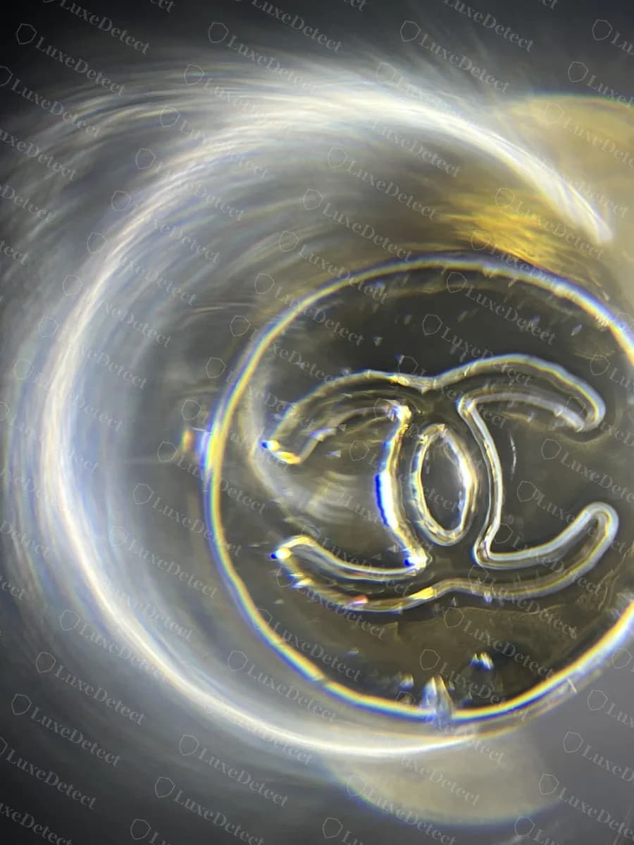 Counterfeit Chanel brooch safety catch photographed under a loupe, the CC engraving copied onto the catch top