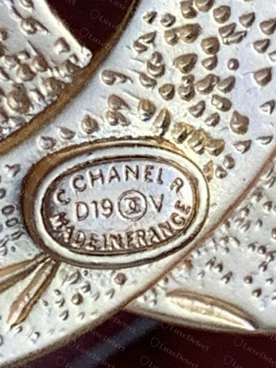 Counterfeit Chanel CC brooch plaque, the same run-together "MADEINFRANCE" and chunky characters crowding the oval, on a textured back