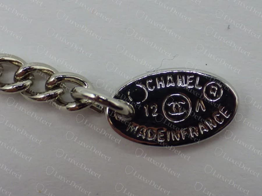 Counterfeit Chanel necklace hang tag, heavy crowded lettering with "MADEINFRANCE" run together as one word and the text pressed against the edge of the oval