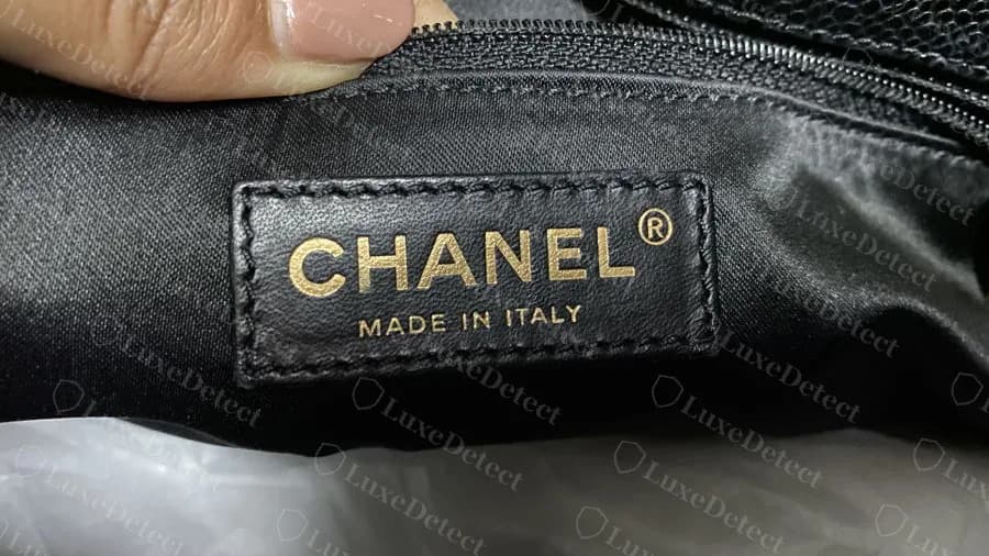 Etiqueta interior de un GST negro original: un parche de piel negra cosido con CHANEL y una marca registrada en lámina dorada encima de MADE IN ITALY