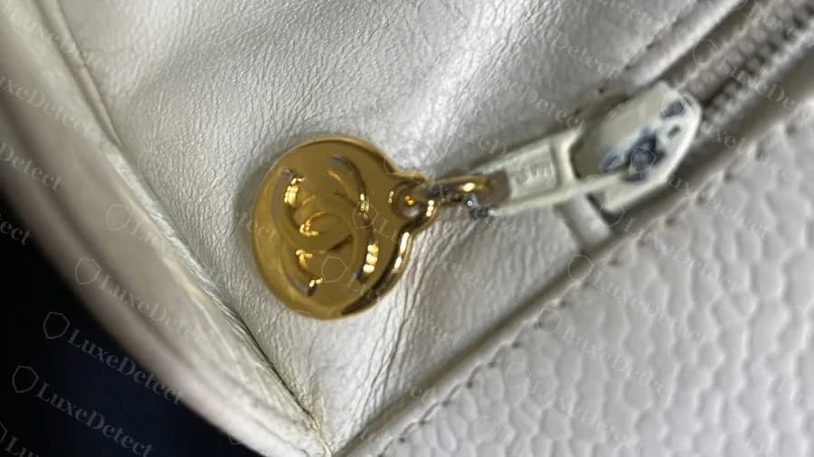 Genuine older white GST zip pull: a small round gold disc with an interlocking CC, hanging from a cream zip slider