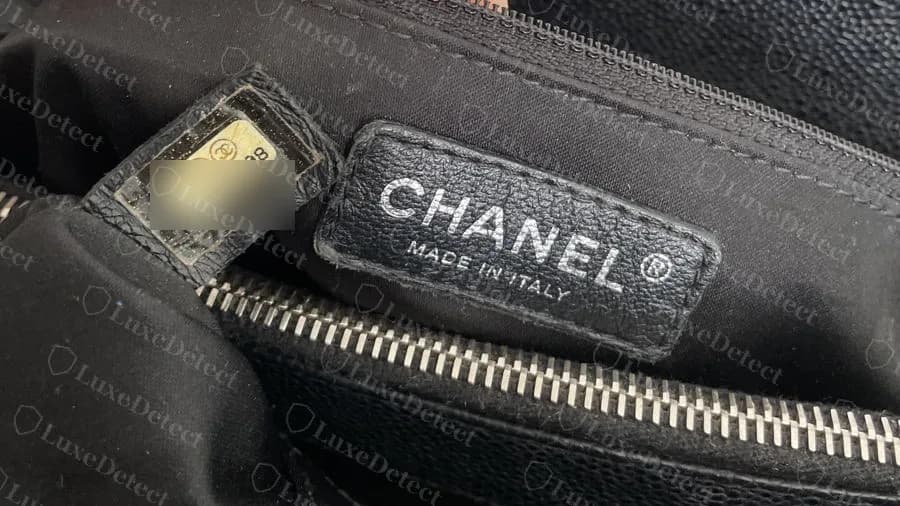 Interior de un GST negro original con una etiqueta adhesiva de serie en una pequeña lengüeta de piel junto al parche CHANEL MADE IN ITALY; los dígitos de la etiqueta están difuminados