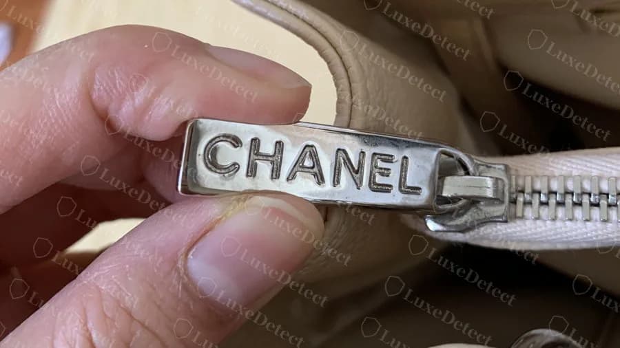 Genuine beige GST zip pull in silver: a flat bar with CHANEL stamped across it, attached to the top-zip slider