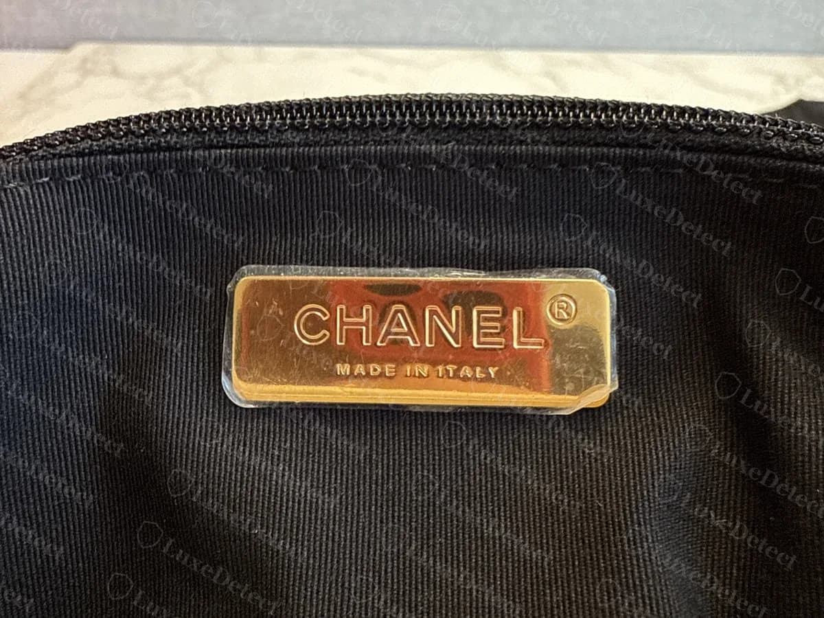 Genuine Chanel 19 interior with a black lining: a gold-tone metal plate reading CHANEL and MADE IN ITALY, below the zip