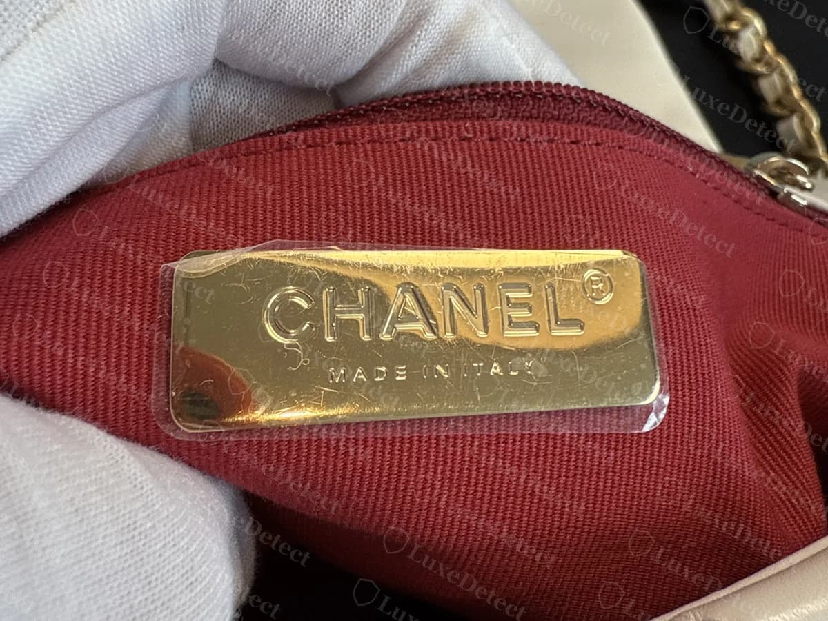 Interior de un Chanel 19 original con forro rojo: una placa metálica en tono dorado grabada con CHANEL, la marca registrada y MADE IN ITALY, colocada sobre el forro