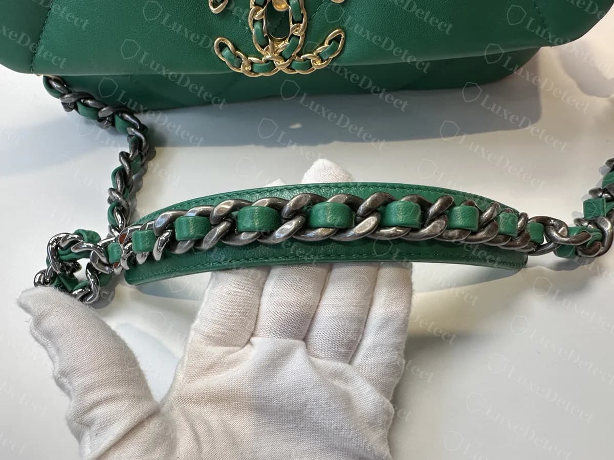 Sección del hombro de un Chanel 19 original verde: una banda acolchada de piel con cadena de rutenio oscuro entrelazada con piel verde, sostenida con una mano enguantada