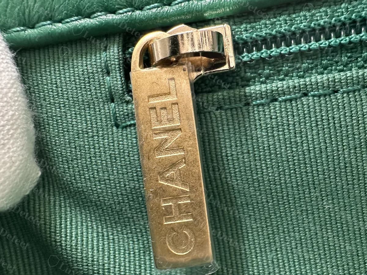 Tirador del cierre interior de un Chanel 19 original verde: un tirador en tono dorado grabado con CHANEL en vertical, sobre el forro verde