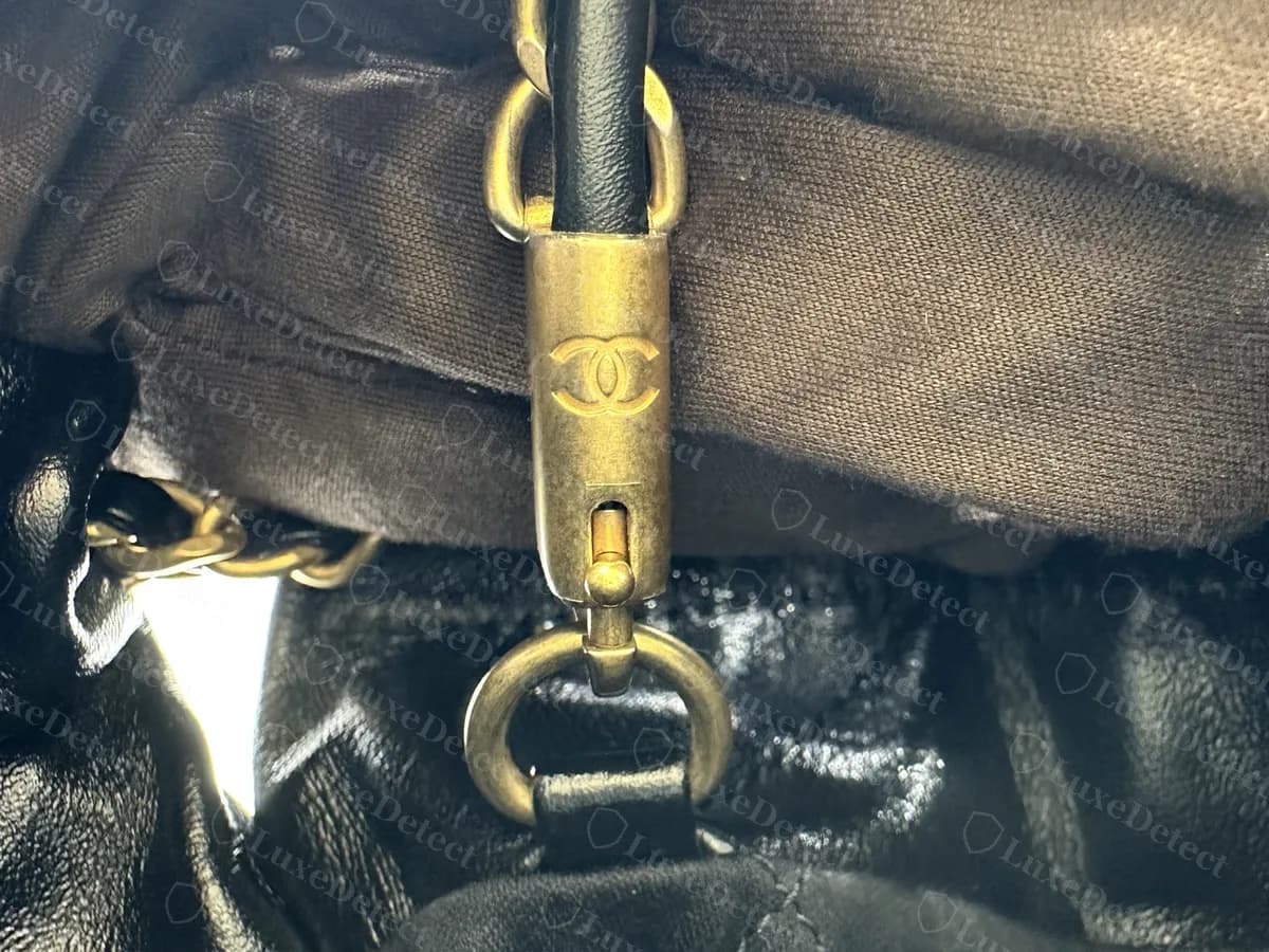 Genuine gold-tone clasp on a Chanel 22: an aged gold hook engraved with the CC logo, next to the leather-wrapped chain end