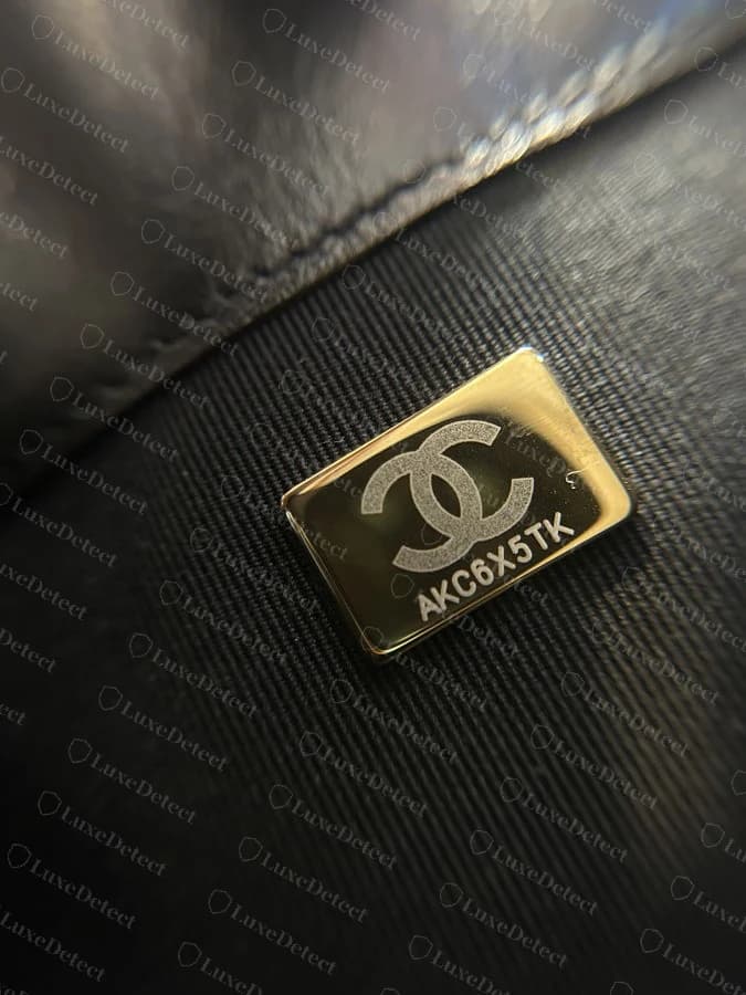 Genuine Chanel microchip authentication plate, CC logo above a unique alphanumeric code, riveted flush into the interior lining