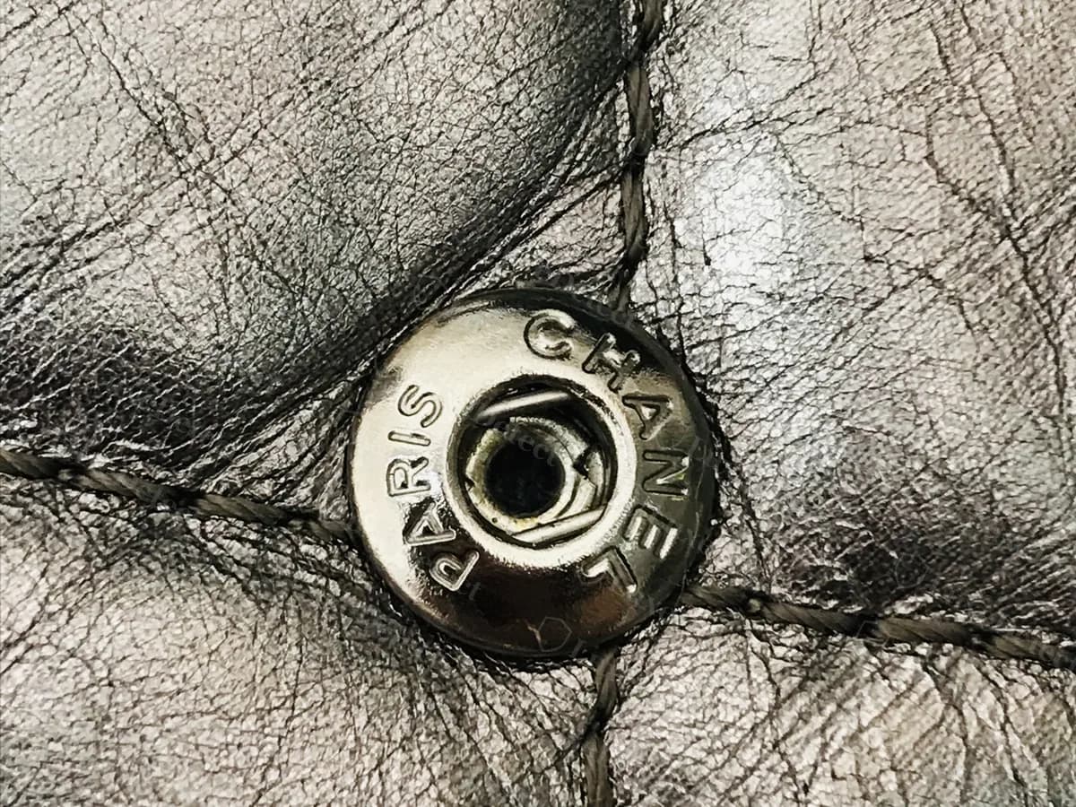 Cuir de veau vieilli argenté métallisé authentique avec un bouton-pression gravé PARIS et CHANEL, serti dans un losange matelassé