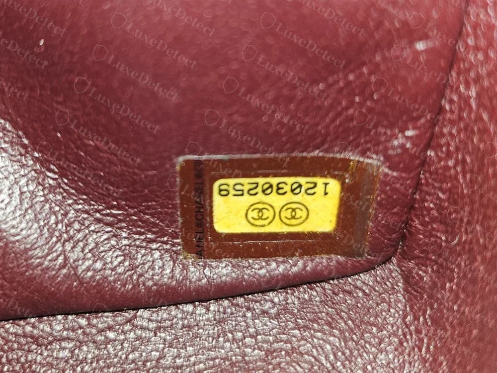 Etiqueta de serie original amarillo dorado dentro del bolso: dos círculos con CC y un número de ocho dígitos, en un marco marrón sobre piel burdeos
