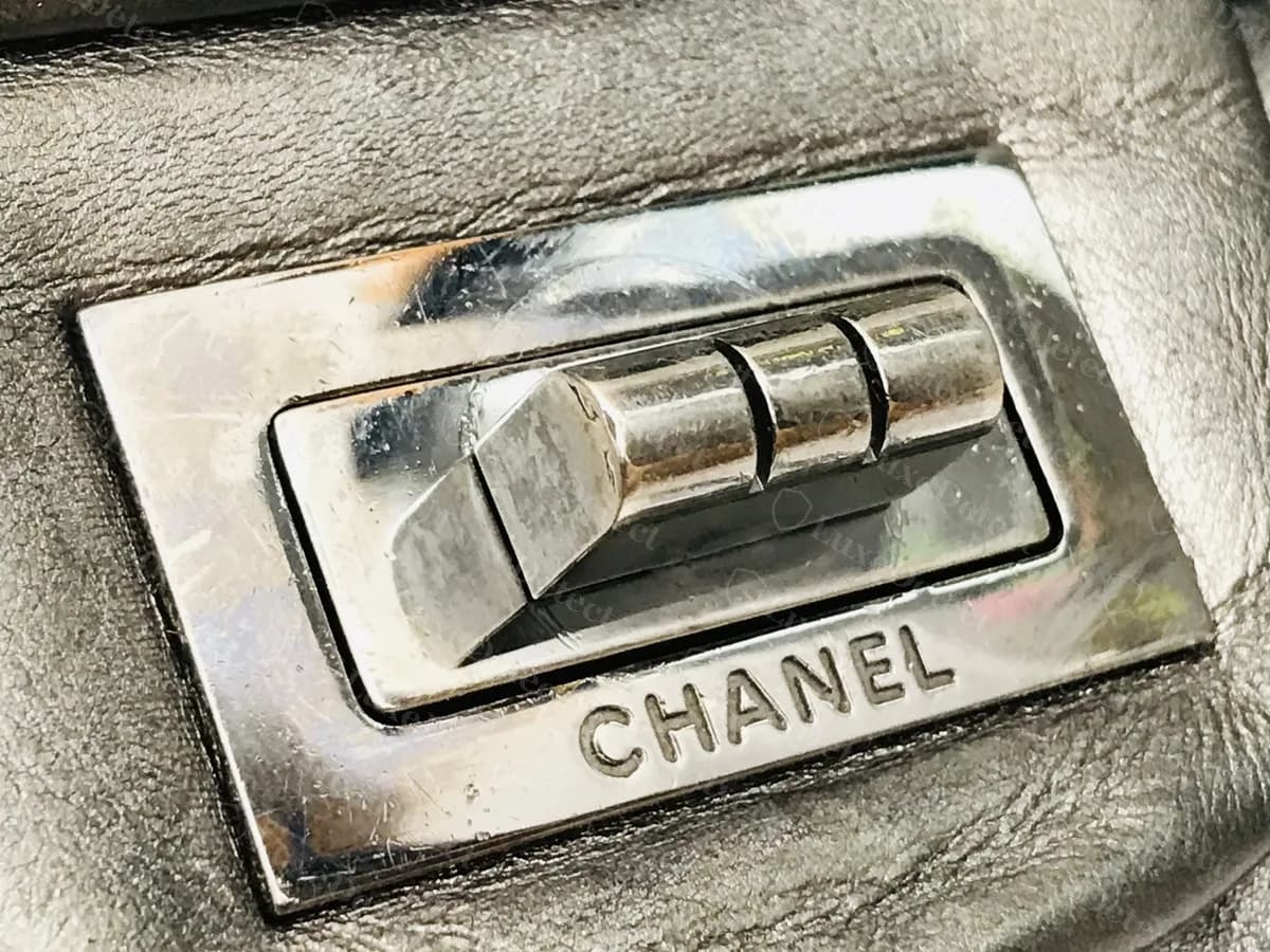 Vue rapprochée d’un fermoir Mademoiselle authentique en argent poli : le loquet à trois barres dans son cadre, avec CHANEL gravé en dessous