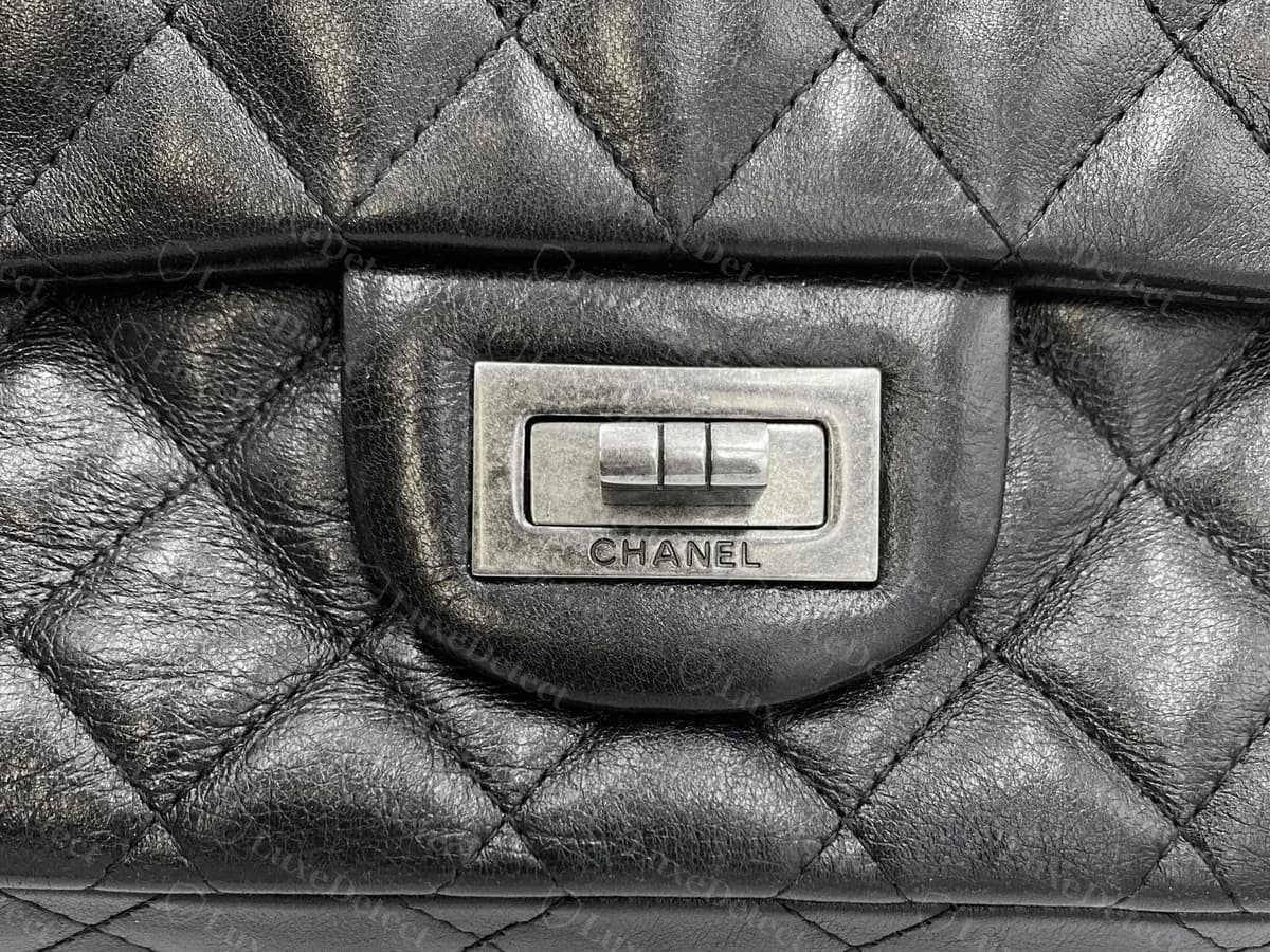 Chanel 2.55 original de piel de becerro envejecida negra: un cierre rectangular Mademoiselle con tres barras deslizantes y CHANEL grabado debajo, sobre piel acolchada arrugada