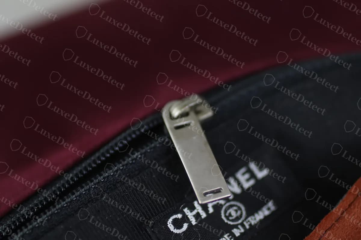 Intérieur de Reissue authentique : une tirette métallique rectangulaire et l’impression CHANEL et MADE IN FRANCE sur la doublure noire en dessous