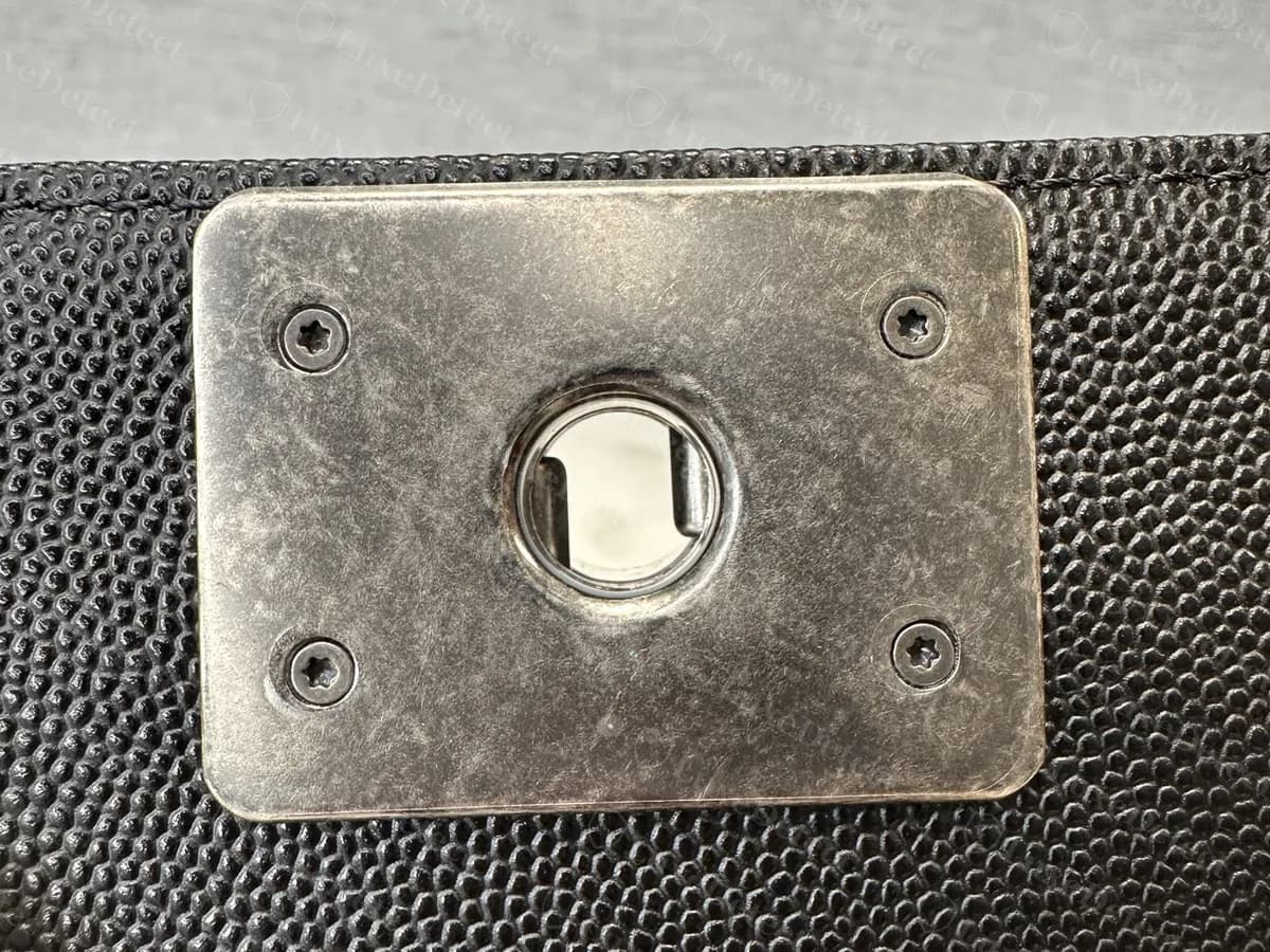 Parte inferior del cierre en la solapa de un Boy original de piel caviar negra: una placa metálica rectangular sujeta con cuatro tornillos pequeños con una abertura en el centro