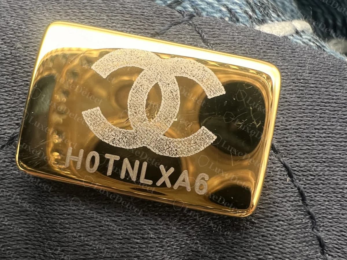 Genuine Chanel microchip plate: a polished gold rectangle on a dark lining with a frosted CC logo and an 8-character code under it
