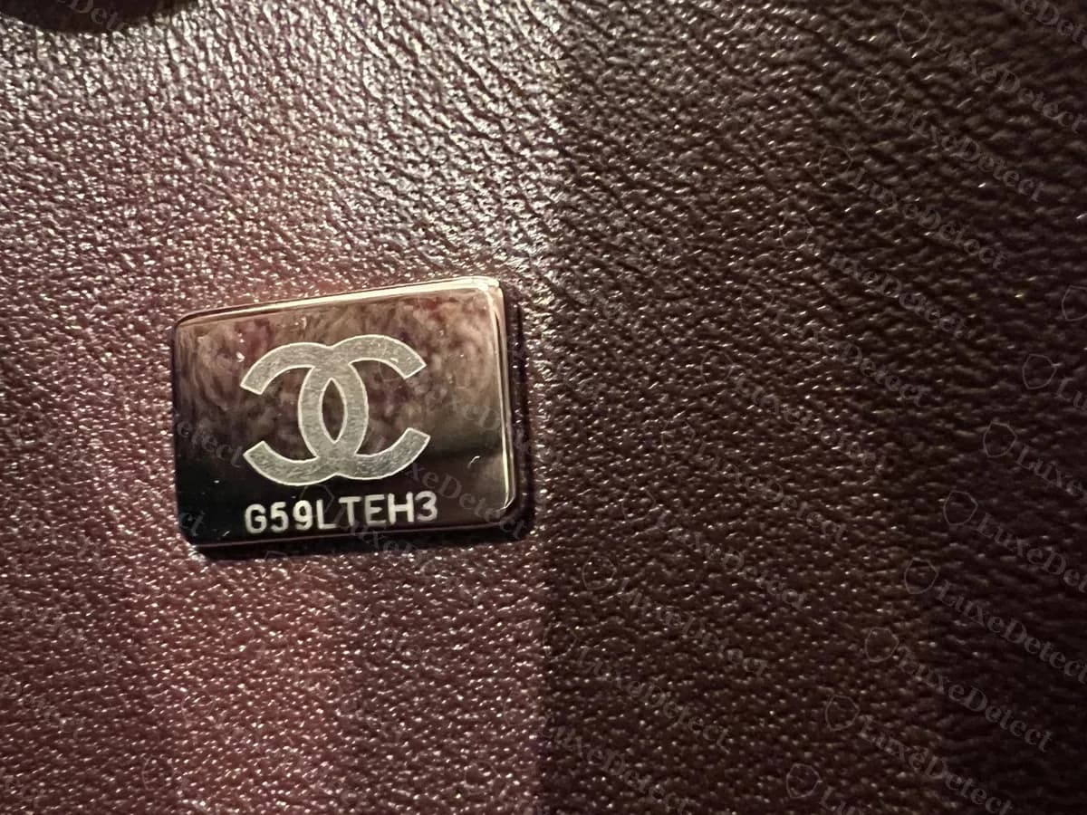 Plaque à puce Chanel authentique ton argent : un rectangle poli sur une doublure en cuir bordeaux, le logo CC au-dessus d'un code de 8 caractères
