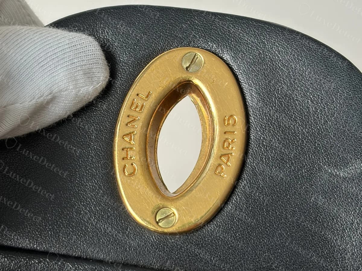 Maxi flap original de piel de cordero negra con una placa dorada ovalada dentro de la solapa, grabada con CHANEL y PARIS y sujeta con dos tornillos