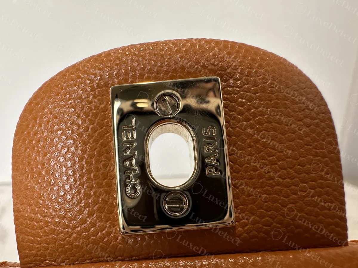 Echte Verschlussplatte einer Classic Flap von der Innenseite der Klappe: eine rechteckige Platte mit CHANEL an einer Seite, PARIS an der anderen und zwei Schlitzschrauben um eine ovale Öffnung