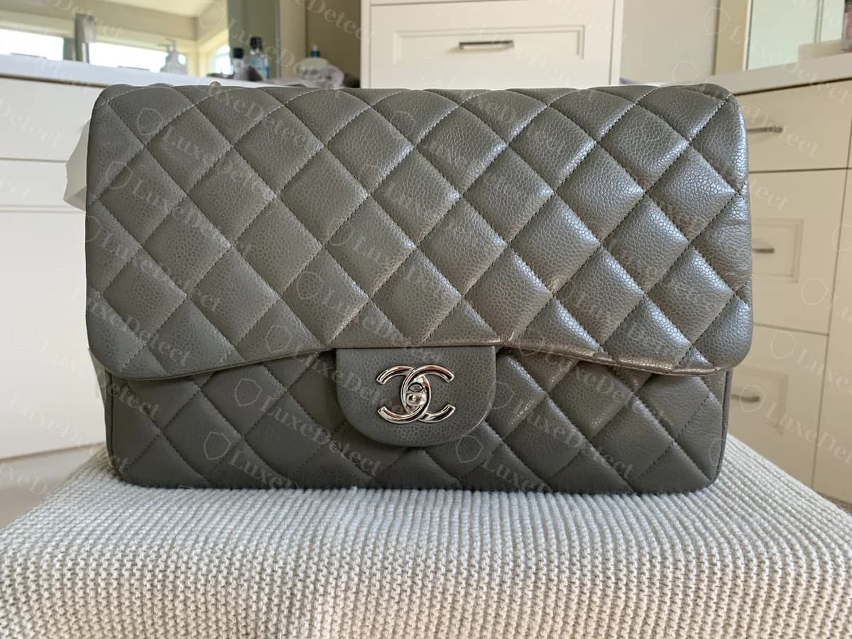 Chanel Classic Flap jumbo de solapa simple original, en piel caviar gris con herrajes plateados, fotografiado de frente sobre un taburete