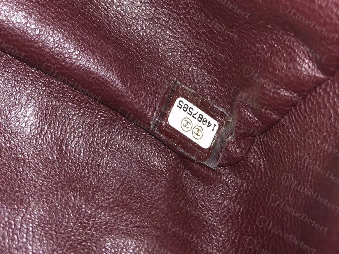 Etiqueta original dentro de un bolso flap con forro burdeos: dos círculos con CC encima del número 14087585, bajo una cubierta de plástico transparente