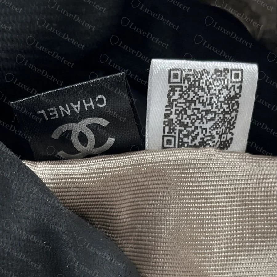 Counterfeit Chanel Deauville — a black-and-white fabric "CHANEL" and QR-code tag stitched permanently into the interior seam near the handle base
