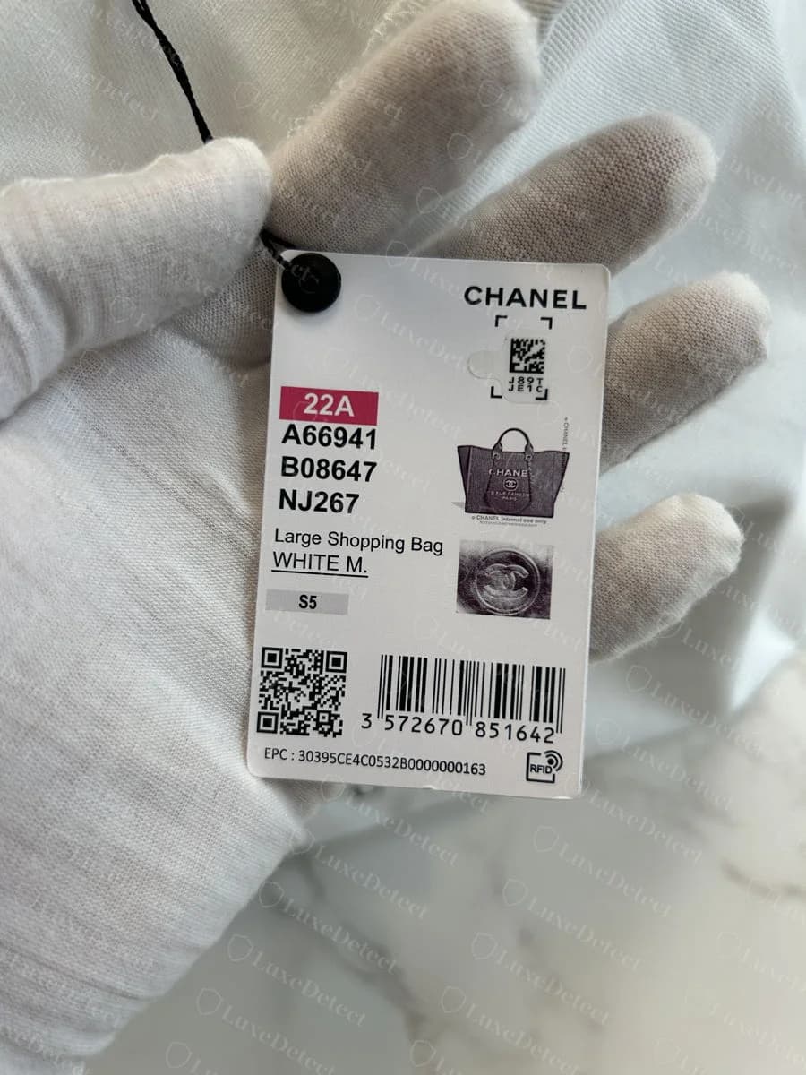 Genuine Chanel retail swing tag — printed CHANEL branding, a small QR/datamatrix code, RFID icon with EPC number, barcode, and style reference numbers, on a detachable cardstock tag