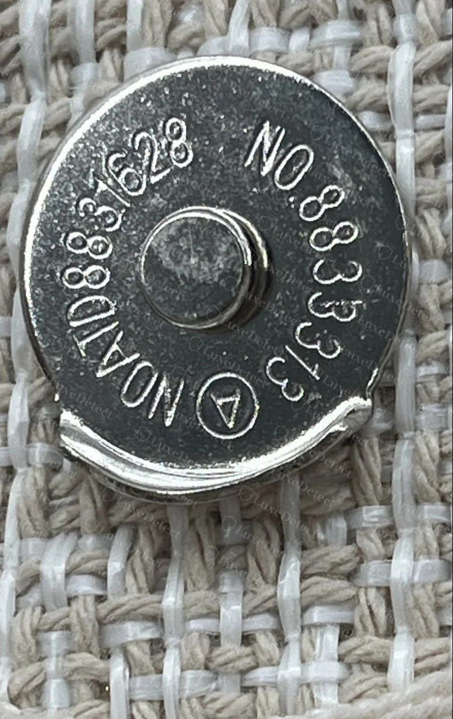 Counterfeit Chanel Deauville — the magnetic snap closure stamped with a generic hardware-supplier part number instead of "CHANEL" or a blank finish