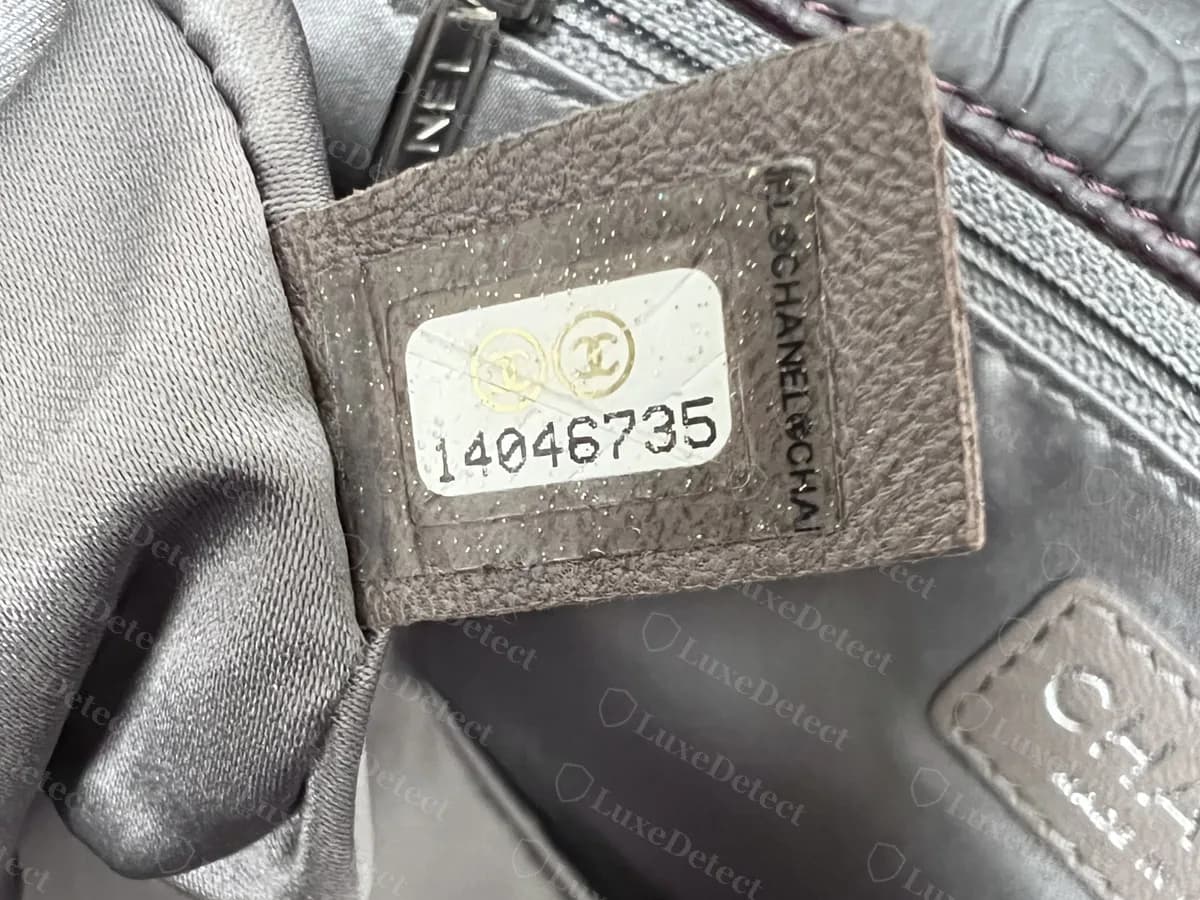 Echter Chanel-Seriennummern-Sticker mit achtstelliger Nummer: zwei CC-Kreise über 14046735, goldene Sprenkel in der Folie und „CHANEL“ senkrecht am rechten Rand, auf einem Lederstreifen in der Tasche