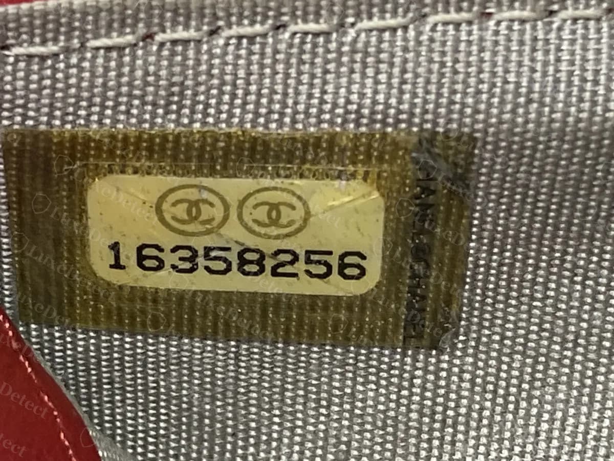 Etiqueta de serie original de Chanel dentro de una cartera: dos círculos con CC entrelazadas encima de un número de serie de 8 dígitos, sobre un parche de película de tono dorado, con "CHANEL" en vertical a lo largo del borde derecho