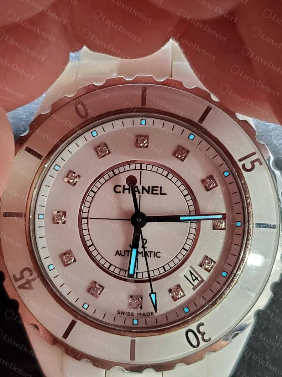 Detail of an authentic J12 dial, "CHANEL" and "J12 AUTOMATIC" in the house's standard typeface, diamond hour markers evenly set.