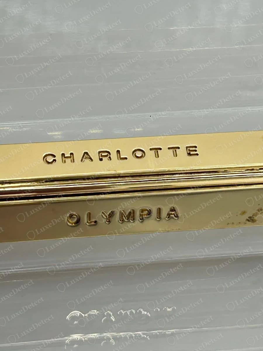 Echte Charlotte-Olympia-Acryl-Clutch mit einer goldenen Scharnierleiste, oben mit CHARLOTTE und unten mit OLYMPIA in weit gesetzten Großbuchstaben graviert