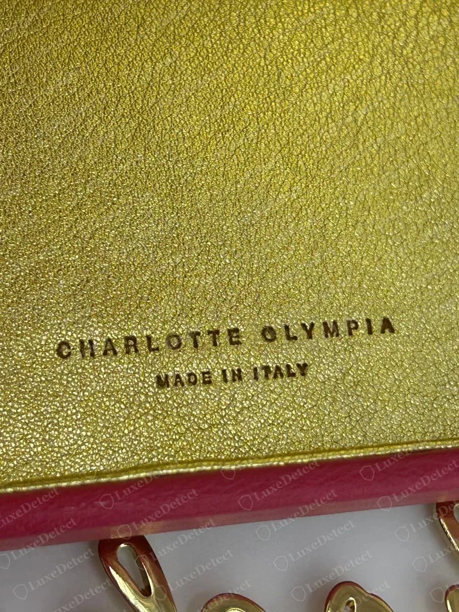 Echtes metallisch goldenes Charlotte-Olympia-Lederfutter mit den Stempeln CHARLOTTE OLYMPIA über MADE IN ITALY, über der rosa Lederkante einer Clutch