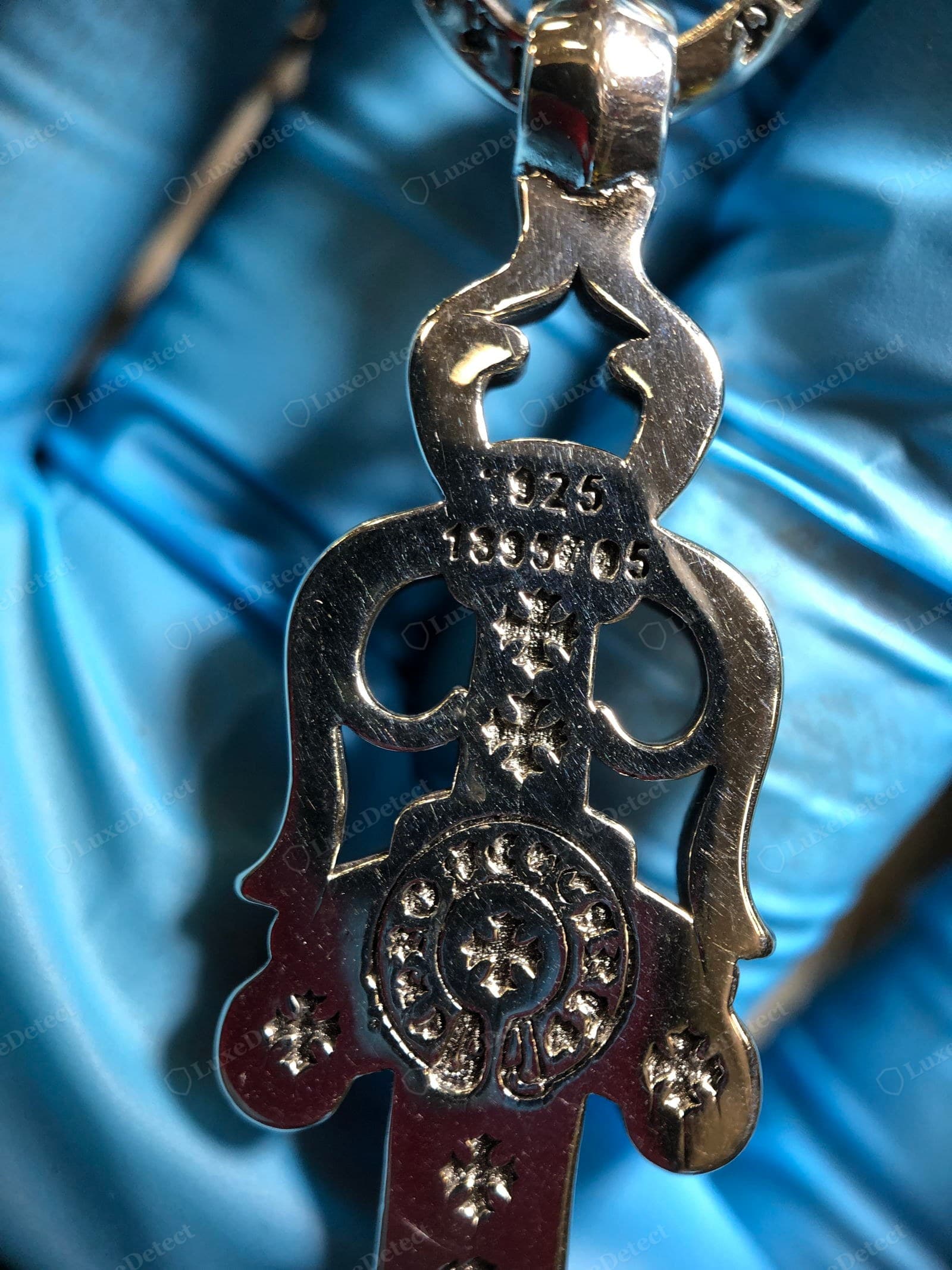 Counterfeit Chrome Hearts cross — the reverse of a fake cross: bright mirror-white with no patina, the engraved CH crosses shallow, identical and stamped rather than cast, a crude "925 1995" hallmark and hairline plating scratches