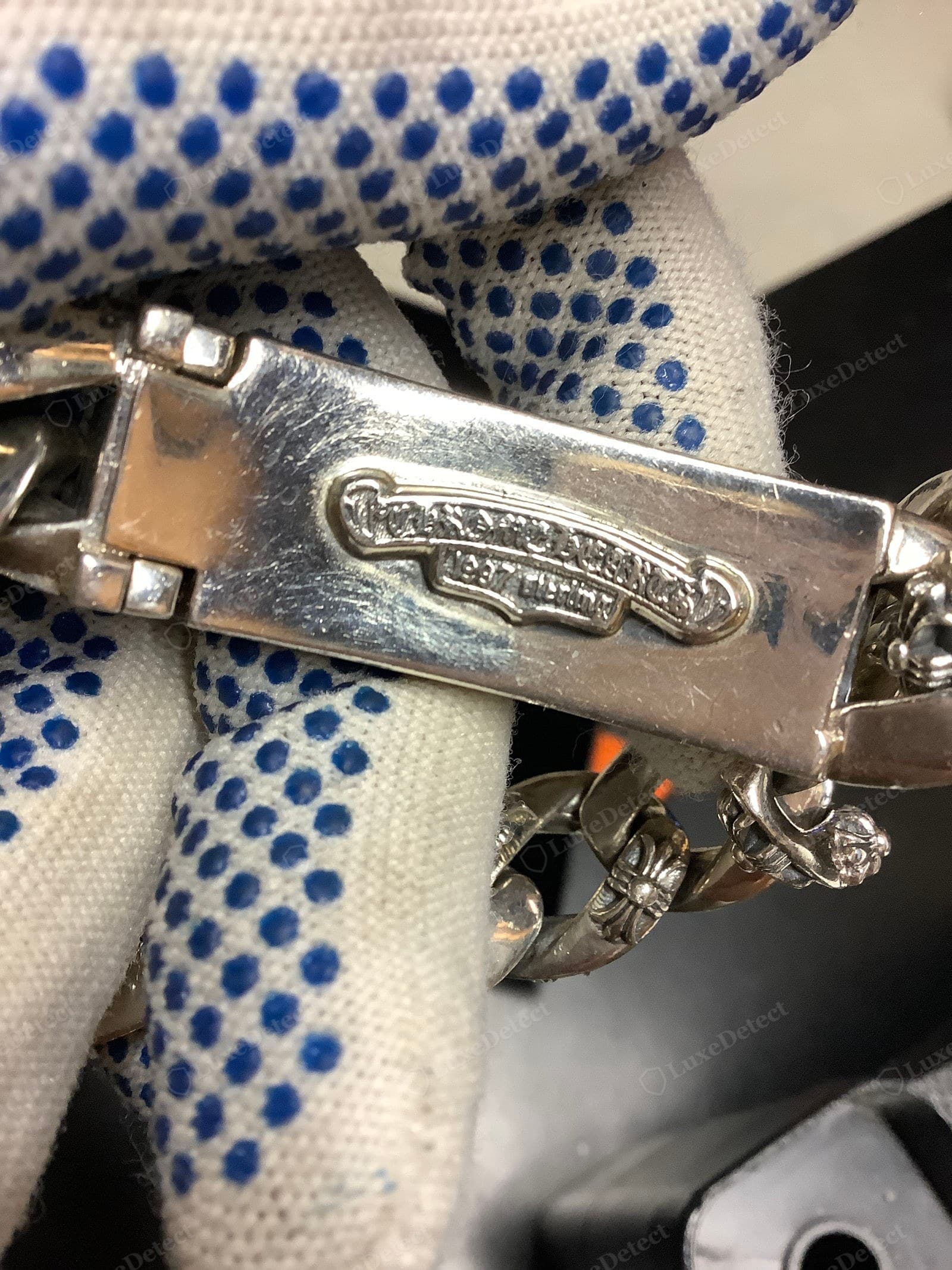 Counterfeit Chrome Hearts hallmark — a raised "CHROME HEARTS / 1997 STERLING" scroll cartouche on a box clasp that is over-bright and heavily scratched, the scroll shape slightly wrong and the metal showing no patina