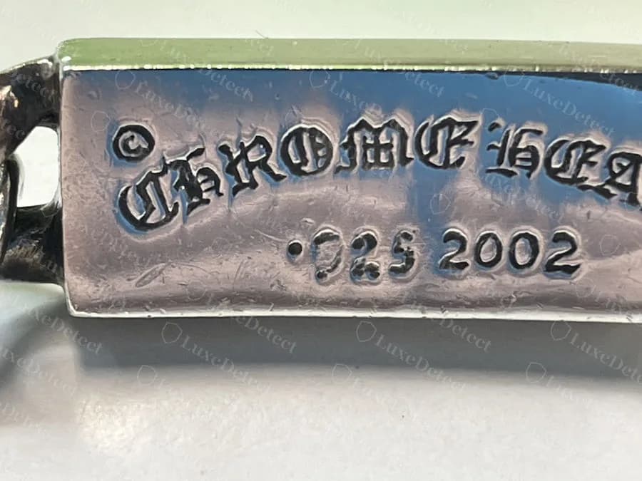 Counterfeit: the reverse of a fake Chrome Hearts ID bracelet plate, "CHROME HEARTS .925 2002" with heavy blotted blackletter that runs together and a ".925" whose 9 and 2 are malformed
