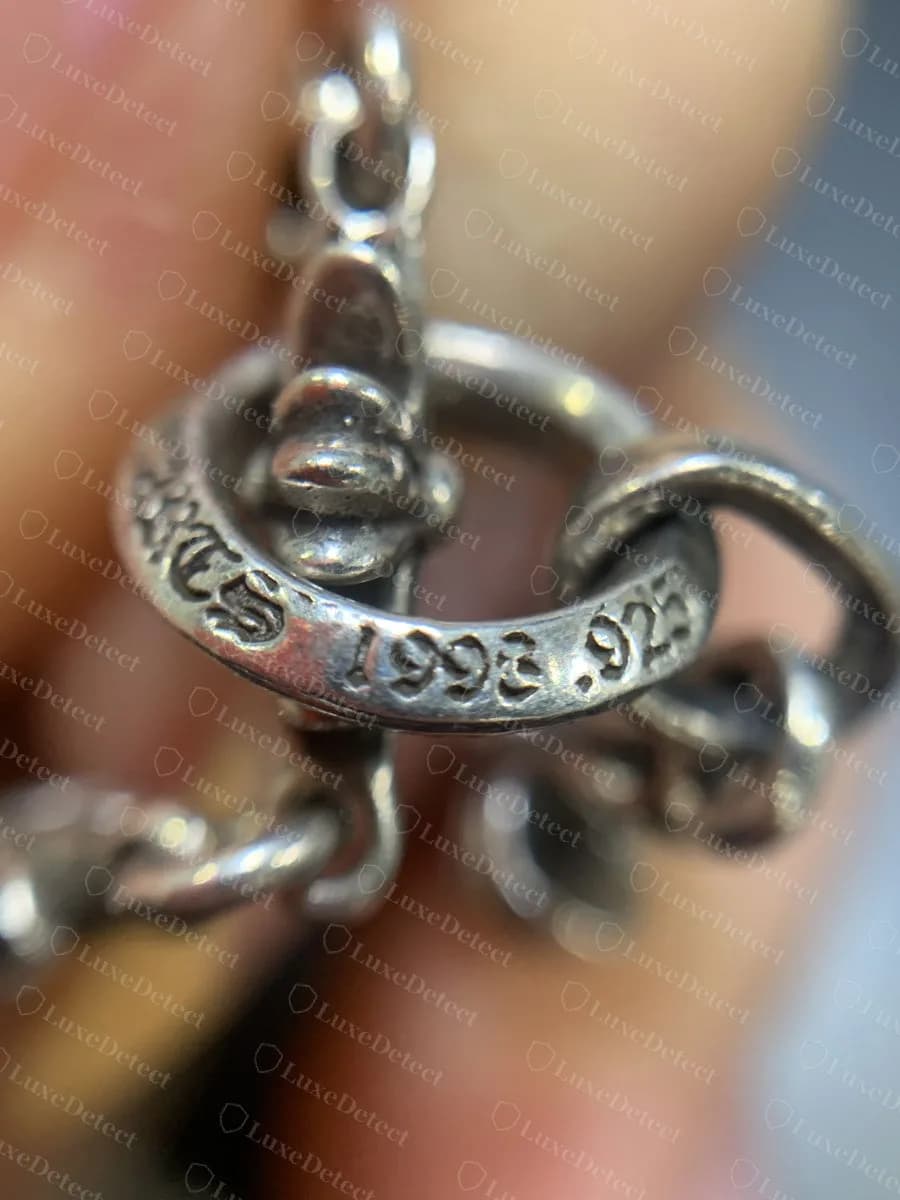 Original: una anilla abierta con sello en un collar genuino de Chrome Hearts, la letra gótica y "1993 .925" rodeando el exterior de una anilla gruesa unida a un eslabón de flor de lis