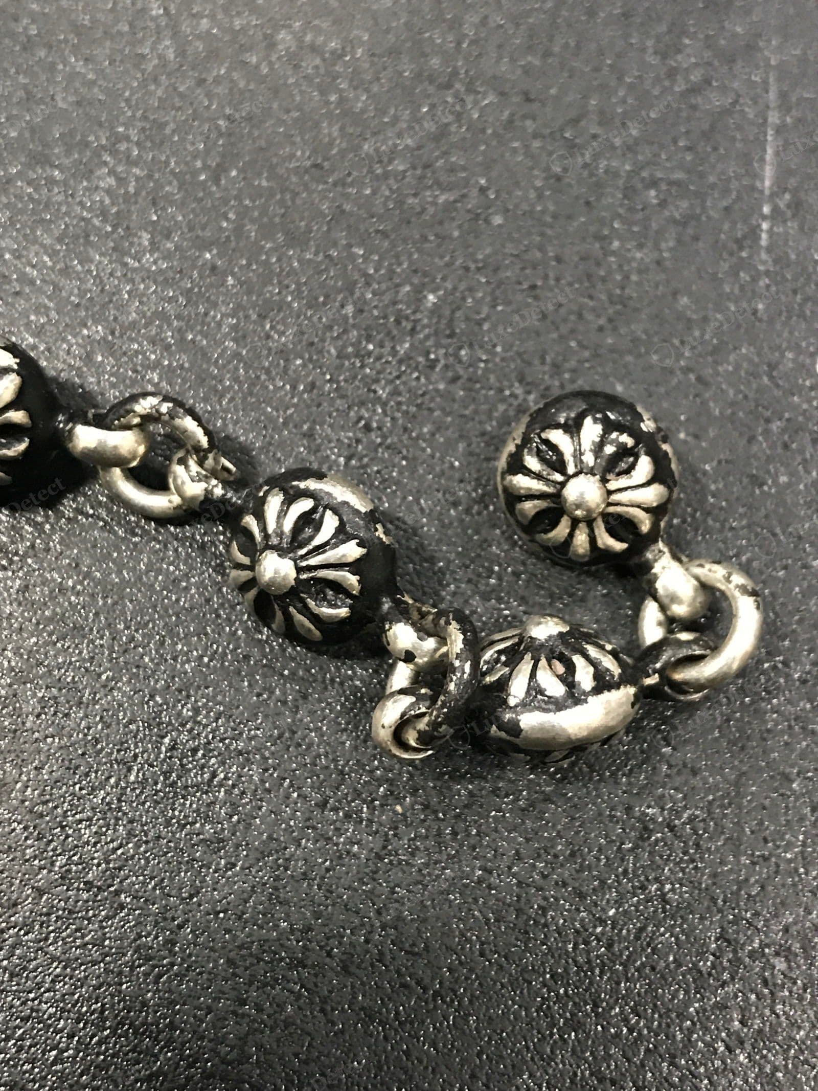 Genuine Chrome Hearts silver — cross-ball beads on a bracelet, each bead cast with the CH floral-cross motif, warm grey sterling tone with oxidised patina deep in the recesses, hand-linked with figure-8 connectors