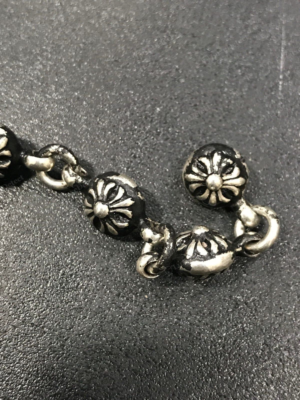Prata Chrome Hearts original — contas de esfera com cruz em uma pulseira, cada conta fundida com o motivo floral-cruz CH, tom quente acinzentado de prata de lei com pátina oxidada no fundo dos recessos, unidas à mão por conectores em forma de 8