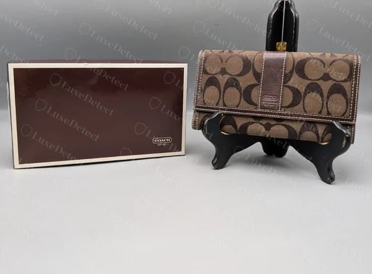 Carteira Coach Signature mais antiga ao lado de uma caixa Coach, que traz uma pequena marca COACH e EST. 1941