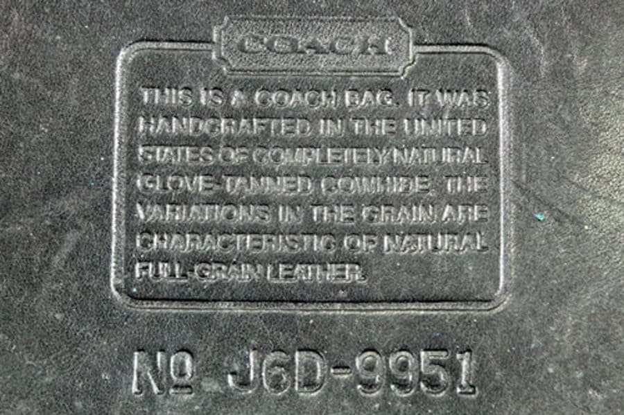 Counterfeit Legacy creed patch, serial J6D-9951. The COACH wordmark and box border are still crisp, but the paragraph beneath has gone soft and mushy, the letters bleeding into each other.